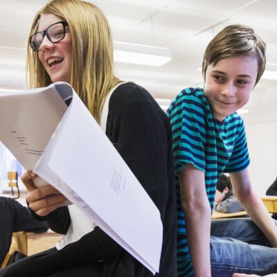 Tre elever i klassrum läser. Två sitter på bänken.