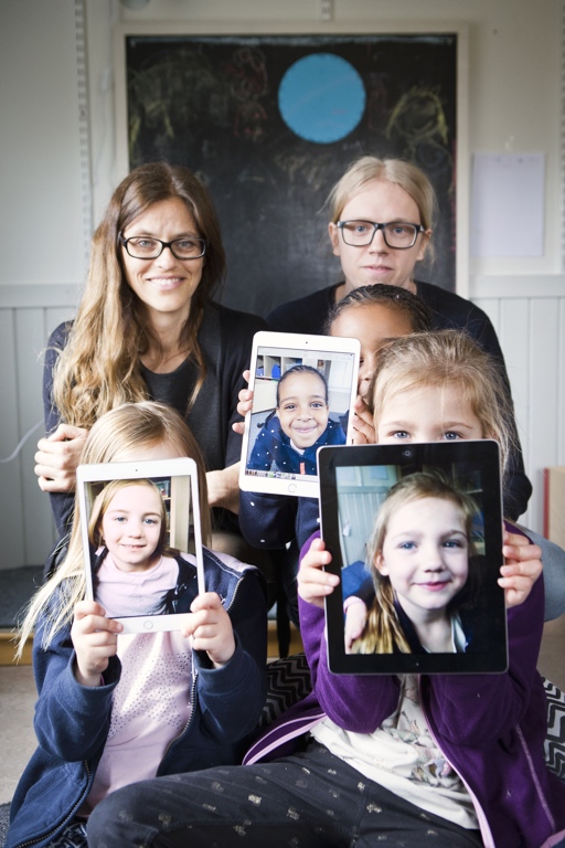 Tre barn som håller upp ipad med bild på sig själva. Och två pedagoger.
