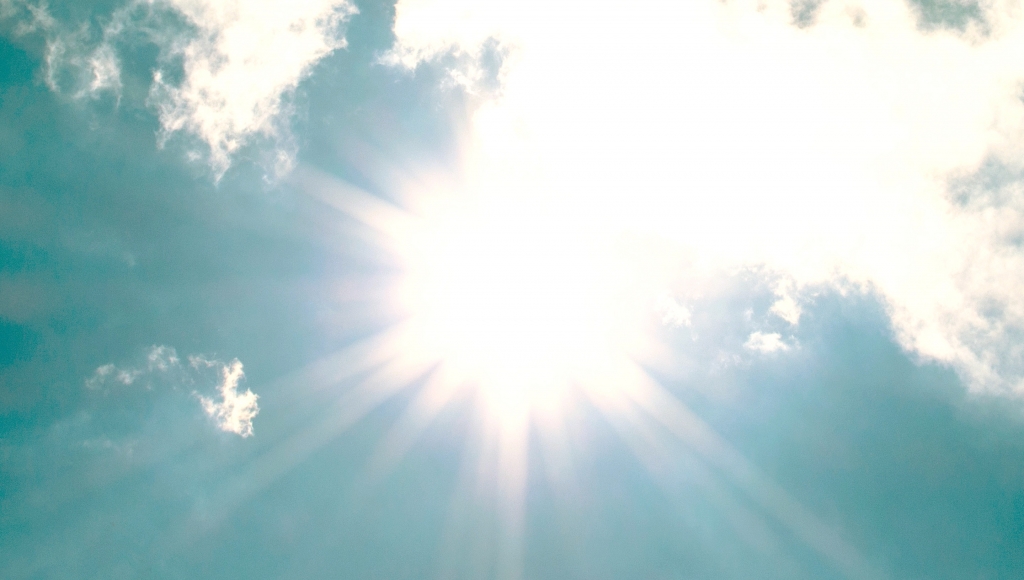stark sol på blå himmel med tunna moln