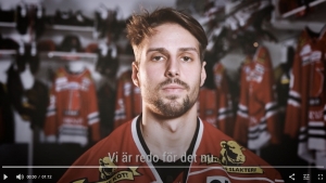 hockeyspelare i röd tröja sitter i omklädningsrummet och tittar in i kameran