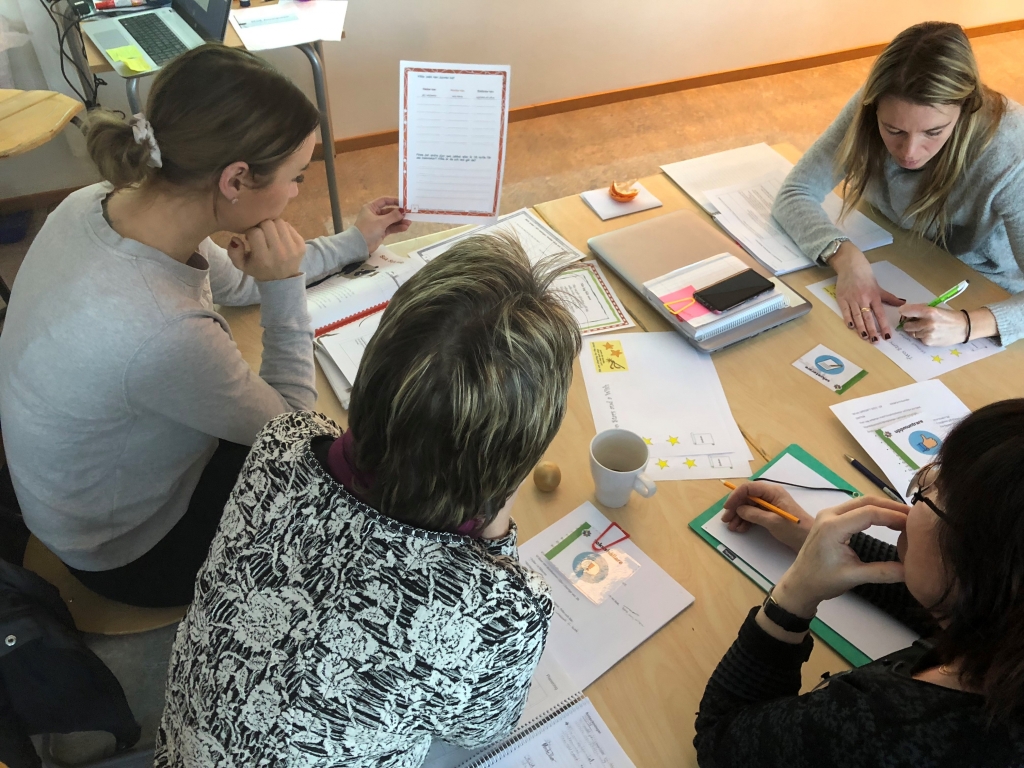 Fyra lärare arbetar tillsammans runt ett bord med mappar, papper, pennor och kaffekoppar.