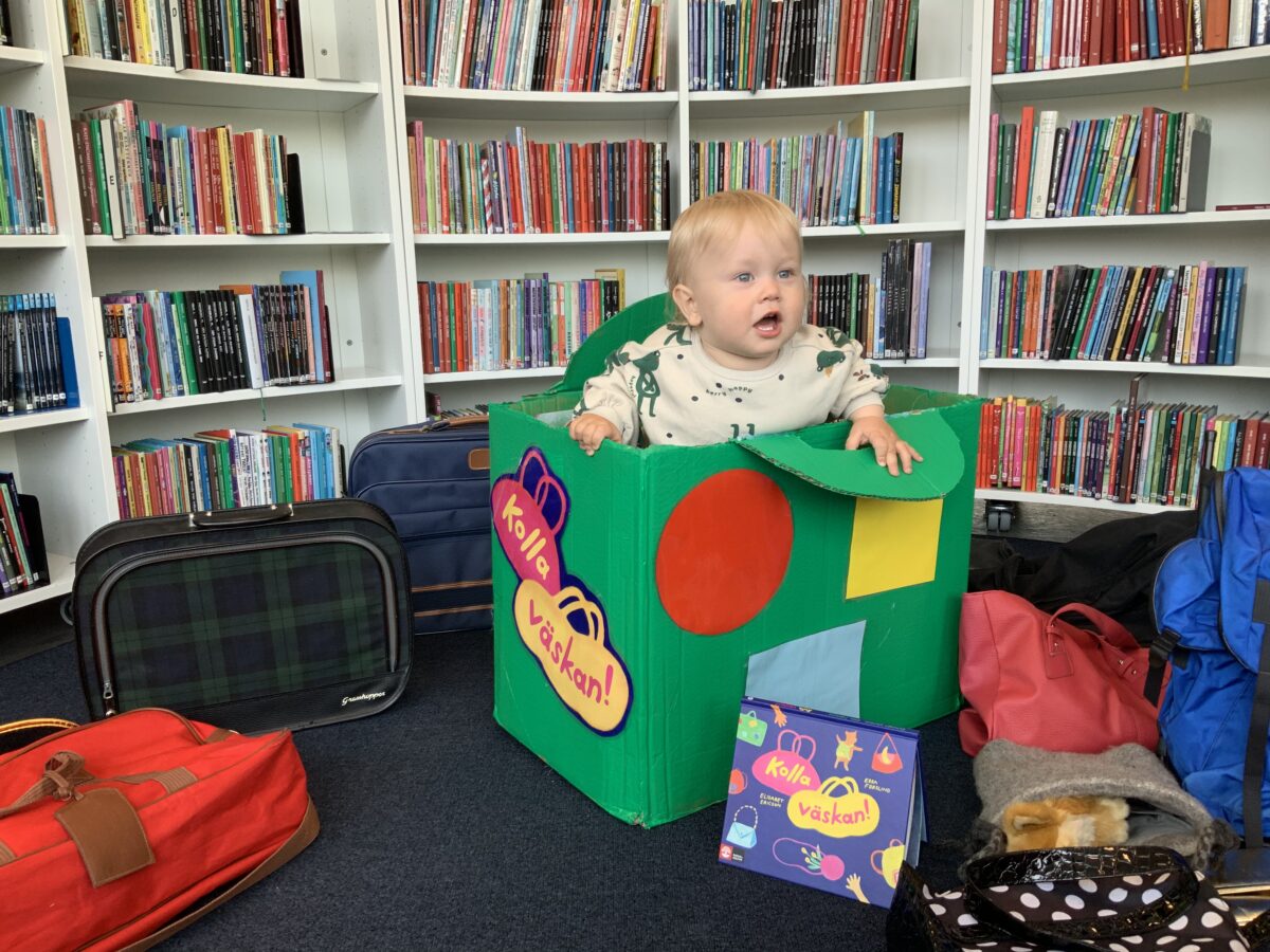 Ett barn som sitter i en stor grön väska på biblioteket.