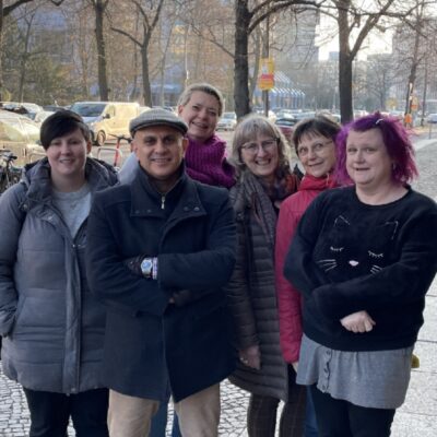Sex personer står på en kullerstensväg i en stad och tittar mot kameran.